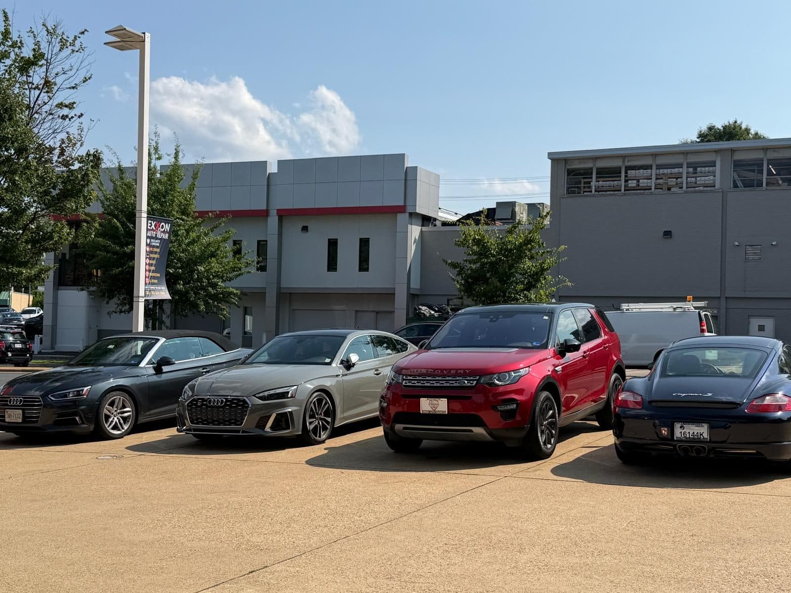 Customer cars parked in the lot: two Audis, a red Land Rover Discovery Sport and a Porsche Cayman S, all on Virginia plates, beside an Exxon Auto Repair banner